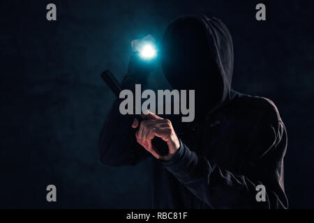 Bewaffneter Raub, Kriminelle mit Hoodie holding Gun und Fackelschein und angreifenden in dunklen, Low Key selektiven Fokus Stockfoto