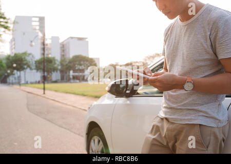 Junge Mann steht in der Nähe des elektrischen Auto und schaut auf dem Smartphone. Der mietwagen wird der Ladevorgang an der Ladestation für Elektrofahrzeuge. Ca Stockfoto