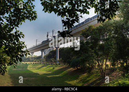 Anzeigen von erhöhten u-Struktur von Astha Kunj Park in der Nähe von Nehru Place von Bäumen, mit der U-Bahn Richtung Badarpur, New Delhi, Indien gerahmt Stockfoto