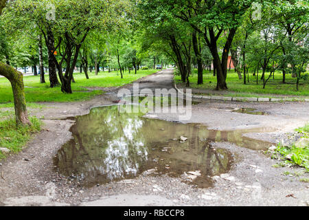 Riwne, Ukraine Rowno Stadt in der westlichen Ukraine outdoor Green Park im Sommer mit nassen regen Pfütze gebrochen heruntergekommenen alten sowjetischen Bürgersteig Weg, niemand, regnerischen Stockfoto