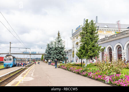 Riwne, Ukraine - 25. Juli 2018: Eisenbahn Eisenbahn Schienen mit Bahnhof Gebäude Straße Straße in der westlichen Ukraine, Stromleitungen, Menschen zu Fuß in Stockfoto