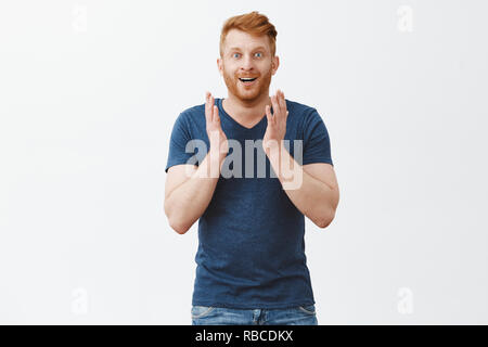 Mit schönen Landschaft verzaubern. Erstaunt und glücklich gut aussehende rothaarige Mann mit Borsten in den blauen T-Shirt, die Palmen an der Kamera sehr zufrieden und begeistert, unter Eindruck über graue Wand anstarren Stockfoto