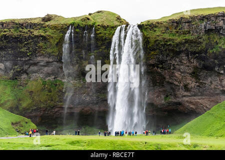 Seljalandsfoss, Island Wasserfall mit weißen Wasser fallen aus Cliff in Grün bemoosten Sommer felsige Landschaft und Menschen zu Fuß auf der Spur Stockfoto