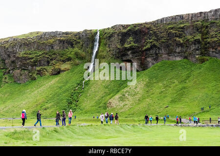 Seljalandsfoss, Island - 14. Juni 2018: Wasserfall mit weißen Wasser von Klippe in Grün bemoosten Sommer felsige Landschaft und Menschen zu Fuß auf Trai Stockfoto