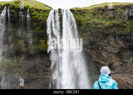 Nahaufnahme der Wasserfall Seljalandsfoss, Island mit Wasser von Klippe in Grün bemoosten Sommer und zurück von einer Frau, die an der Ansicht Suchen Stockfoto