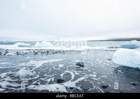 Landschaft Blick auf viele blaue Gletscher Eisberge in Jokulsaron Lagune See Diamond Beach in Island mit schwarzem Sand und Wellen ufer Wasser Stockfoto