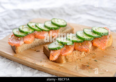Sandwiches mit Brot, frischem Fisch und in Scheiben geschnittene Gurken mit Gewürzen auf Holz- Fach. Stockfoto