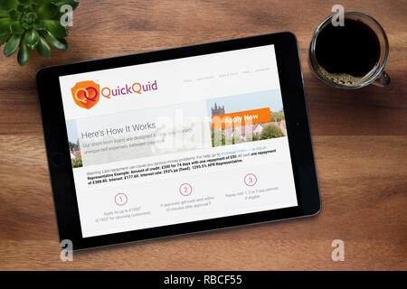 Die Website von QuickQuid ist auf einem iPad Tablet gesehen, auf einer hölzernen Tisch zusammen mit einem Espresso und einem Haus Anlage (nur redaktionelle Nutzung). Stockfoto