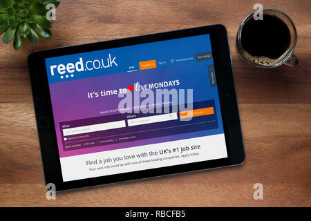 Die Website von Reed.co.uk ist auf einem iPad Tablet gesehen, auf einer hölzernen Tisch zusammen mit einem Espresso und einem Haus Anlage (nur redaktionelle Nutzung). Stockfoto