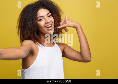 Close-up fröhlicher junger wunderschöne afrikanische amerikanische Frau, eine selfie selbst und Phone Symbol von Hand. Gelbe studio Hintergrund. Platz kopieren Stockfoto