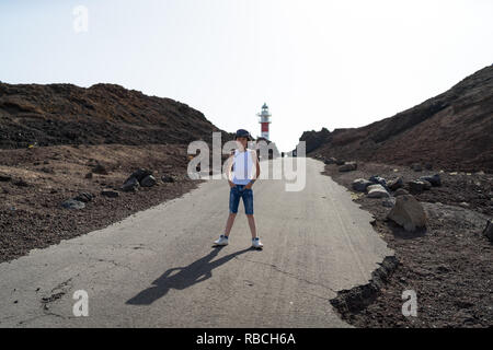 Porträt eines Jungen im vollen Wachstum gegen Leuchtturm auf der felsigen Ufer des Kaps von Teno (Punta de Teno). Teneriffa. Kanarischen Inseln. Spanien. Stockfoto