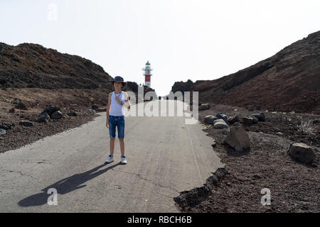 Porträt eines Jungen im vollen Wachstum gegen Leuchtturm auf der felsigen Ufer des Kaps von Teno (Punta de Teno). Teneriffa. Kanarischen Inseln. Spanien. Stockfoto