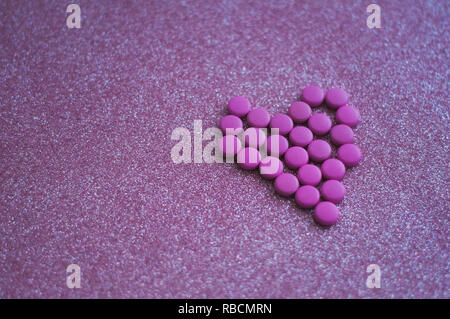 Rosa Pillen in Form eines Herzens auf glitter pink Hintergrund. farbige Drogen. Konzept - Herz-Krankheit, Herz-Kreislauf-Erkrankungen und Medikamente, Kardiologie. Stockfoto