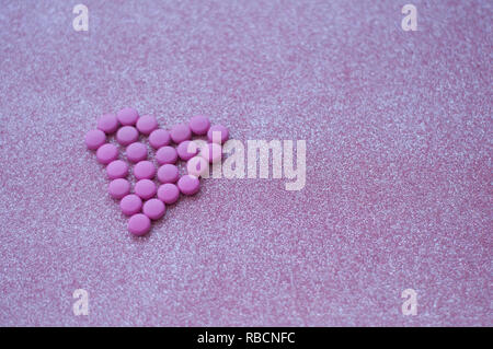 Rosa Pillen in Form eines Herzens auf glitter pink Hintergrund. farbige Drogen. Konzept - Herz-Krankheit, Herz-Kreislauf-Erkrankungen und Medikamente, Kardiologie. Stockfoto