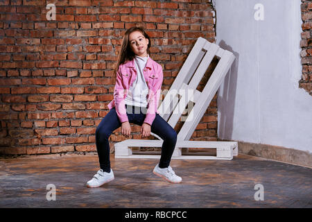 Mädchen Teenager darstellen Bewegung Tanz in Loft im Innenbereich. Schönes Kind brunette wirbt für legere Kleidung, Jugend Stil. Junge hipster 9-13 Jahre in Pink jacket Denim, jeans, Turnschuhe. Stockfoto