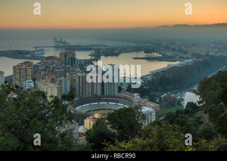 Spanische Stadt Malaga bei Sonnenuntergang. Hafen und der Altstadt mit einem Bull Ring von oben. Gebäude und Schiffe im Hafen gesehen werden kann. in der backgroun Stockfoto