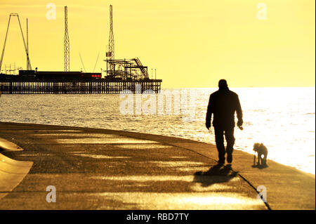 Blackpool, Großbritannien. 9 Jan, 2019. Silhouette der Mann den Hund entlang der Promenade in der Nähe der Pier auf einer ungewöhnlich ruhigen Tag im Januar. Credit: Kevin Walsh/Alamy leben Nachrichten Stockfoto