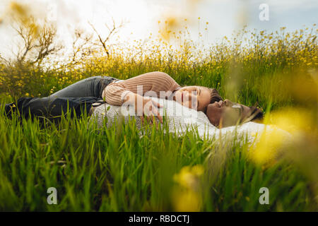 Junge Paare, die auf dem Gras in der Wiese. Entspannt junger Mann und eine Frau, die auf dem Gras im Freien. Stockfoto