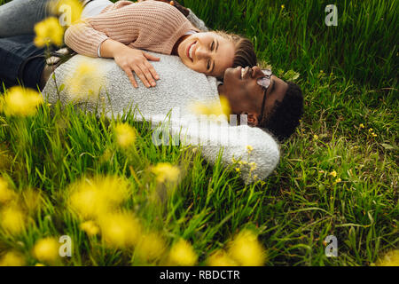Schöne junge Paar liegen im grünen Gras im Freien. Junger Mann und Frau liegen in der blühenden Wiese im Freien. Stockfoto