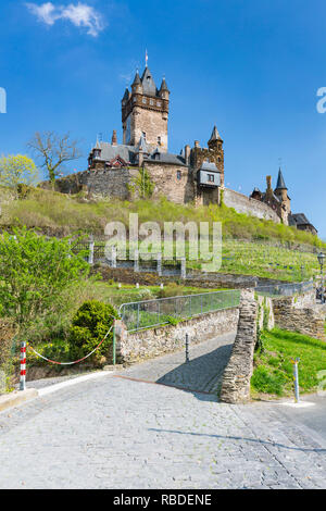 Low Angle Blick auf die berühmte Reichsburg Cochem in der Eifel an der Mosel in Deutschland mit blauem Himmel und gepflasterte Straße aufsteigend in den Vordergrund. Stockfoto