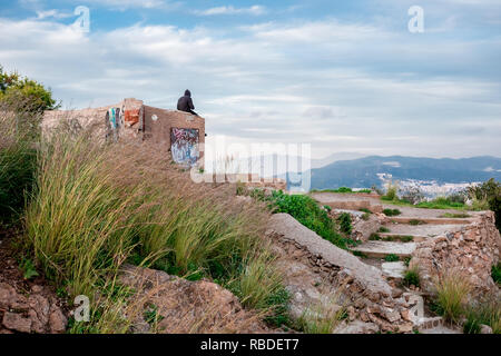 Junge lonely Teenager mit Pullover sitzen auf Berg Blick auf Landschaft während Moody bewölkt Bewölkter Tag Stockfoto