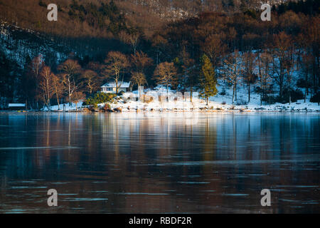 Abendlicher Blick über den zugefrorenen Obersee Rursee mit einem Haus, in der Nähe der Küste im Winter in der Eifel. Stockfoto