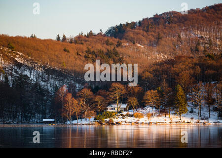 Abendlicher Blick über den zugefrorenen Obersee Rursee mit einem Haus, in der Nähe der Küste im Winter in der Eifel. Stockfoto