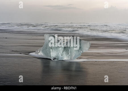 Markante Eisblock auf einem schwarzen Strand mit Surf, mit wieder Wasser Reflexion auf dem nassen Sand, Wellen im Hintergrund rolling - Ort: Island Stockfoto