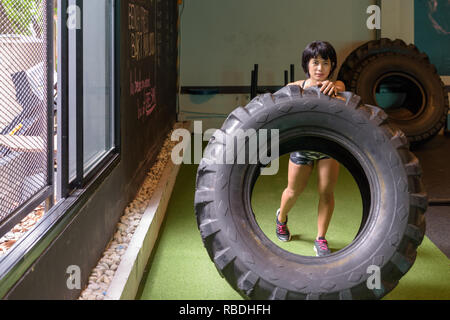 Asiatische fitness Frau drücken und drehen das Rad Reifen im Fitnessstudio Stockfoto