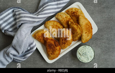 Spanische und Lateinamerikanische fried Empanadas mit Soße auf dem grauen Stein Hintergrund, Ansicht von oben Stockfoto