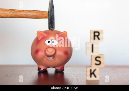 Hand mit einem Hammer über einem Sparschwein und Risiko Wort auf Holzwürfel geschrieben Stockfoto