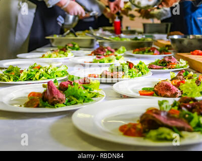 Warmes Roast Beef, frischer Salat und Tomaten serviert auf Weiße Platten. Kochen Master Class, Workshop mit Menschen lernen, wie man zu Kochen rund um den Tisch Stockfoto