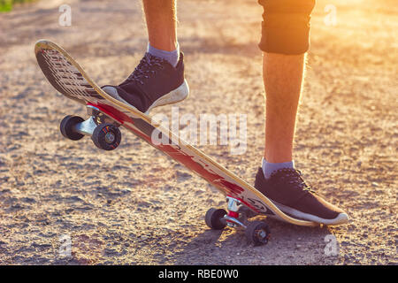 Der Kerl steht auf einem Skateboard ist auf der Straße schöne Muskelaufbau. Stockfoto