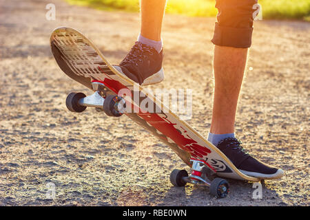 Der Kerl steht auf einem Skateboard ist auf der Straße schöne Muskelaufbau. Stockfoto