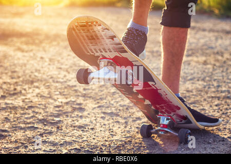 Der Kerl steht auf einem Skateboard ist auf der Straße schöne Muskelaufbau. Stockfoto
