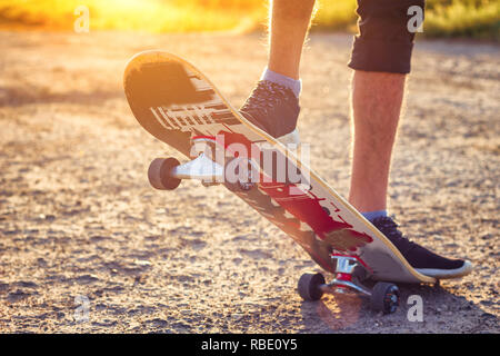 Der Kerl steht auf einem Skateboard ist auf der Straße schöne Muskelaufbau. Stockfoto