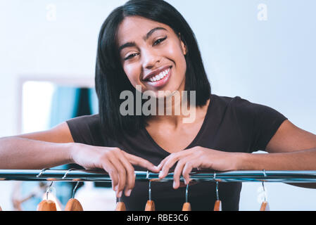 Mein Store. Schöne indische lächelnde Frau stand in der Nähe der Kleiderbügel Stockfoto