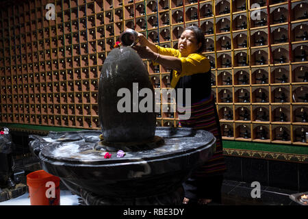 Eine tibetische Frau gießt Wasser über eine Statue der Gottheit Shiva zu einem Hindu Tempel in Woodside, Queens New York City. Stockfoto