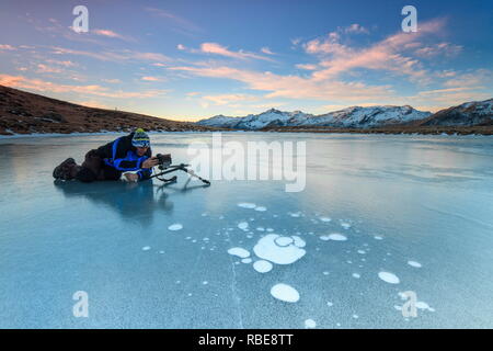 Fotograf in Aktion auf der gefrorenen Oberfläche des Andossi-Sees bei Sonnenaufgang Spluga Tal Valtellina Lombardei Italien Europa Stockfoto