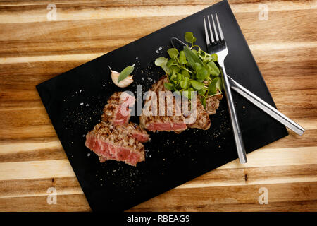 Grundriss der saftigen und saftig seltene rindersteak, mit Brunnenkresse garnieren, auf einer Schiefertafel Platte, mit Messer und Gabel Stockfoto