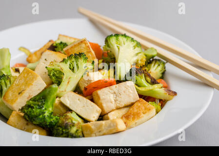 Gegrillter Tofu mit Broccoli und Karotten in weiße Platte mit Stäbchen auf der rechten Seite. Stockfoto