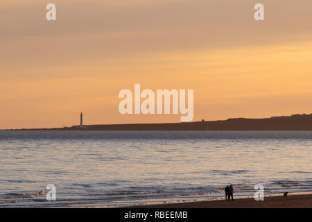 Zwei Leute, die einen Hund in den späten Nachmittag am Strand von St Cyrus mit Blick über Montrose Bay Scurdie Ness Lighthouse Stockfoto