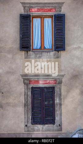 Foto von zwei Verwitterten windows gegen eine verschlissene gelbe Putz an der Wand in der mittelalterlichen Ortschaft Montalcino in der Toskana, Italien. Stockfoto