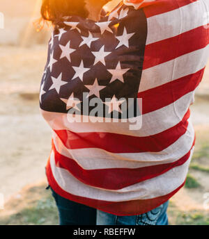 Paar verpackt in der amerikanischen Flagge bei Sonnenuntergang küssen Stockfoto