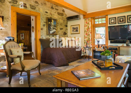 Antike gepolsterten Stuhl und Holz Couchtisch in der neuen Verlängerung innerhalb eines alten ca. 1740 Canadiana fieldstone Cottage style Home Stockfoto