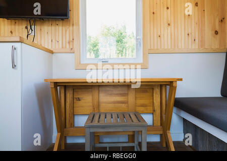 Weißem melamin Küchenschrank und erweiterbare Kiefernholz Esstisch mit Sitzbank im Sitzbereich in einem 8 x 24-Fuß-mobile Mini Haus Stockfoto