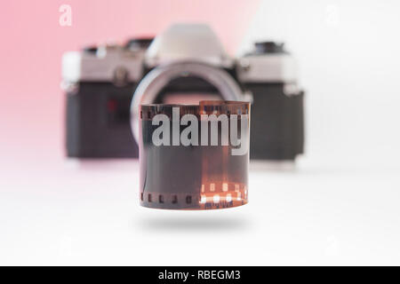 Hochfliegende 35 mm Film Roll mit verschwommenen SLR-Kamera im Hintergrund Stockfoto