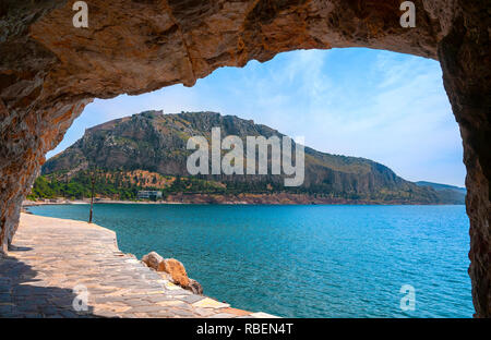 Küstenweg mit großen Felsen Torbogen geben einen Blick auf die Festung Palamidi oder Burg auf dem Acronauplia Halbinsel, Nafplio, Argolis, Peloponnes, Griechenland Stockfoto