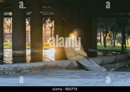 Obdachlose afrikanischer Mann unter der Brücke in der Alten trockenen Fluss und derzeit einen riesigen Park in der Stadt Valencia. Einsamer Mann schlafen im Sitzen. Stockfoto