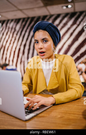 Eine junge Malay asiatische Frau, ist das Schreiben und Arbeiten oder Studieren auf Ihren Laptop in einem Cafe während des Tages. Sie trägt einen Turban Hijab. Stockfoto